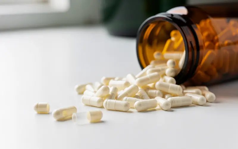 Empty ivory-white two-piece acid-resistant HPMC hard capsules spilling from a tilted amber glass jar